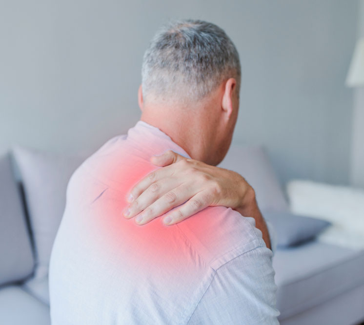 An older man, seen from the back, holds his shoulder joint, which is highlighted in red to indicate pain and inflammation from arthritis.