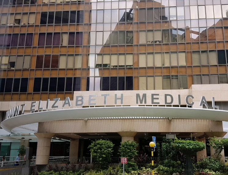 The exterior and main entrance of the Mount Elizabeth Medical Centre, showing the building's sign on a modern awning and its multi-story glass facade.