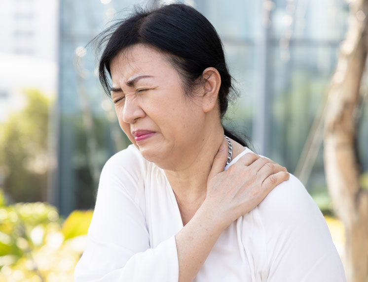 An older woman with an expression of pain holds her shoulder and neck, illustrating the symptoms of a condition like arthritis or a pinched nerve.