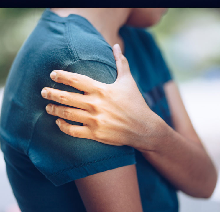 A close-up of a person holding their painful shoulder, illustrating a symptom of an injury or an inflammatory condition like shoulder bursitis.