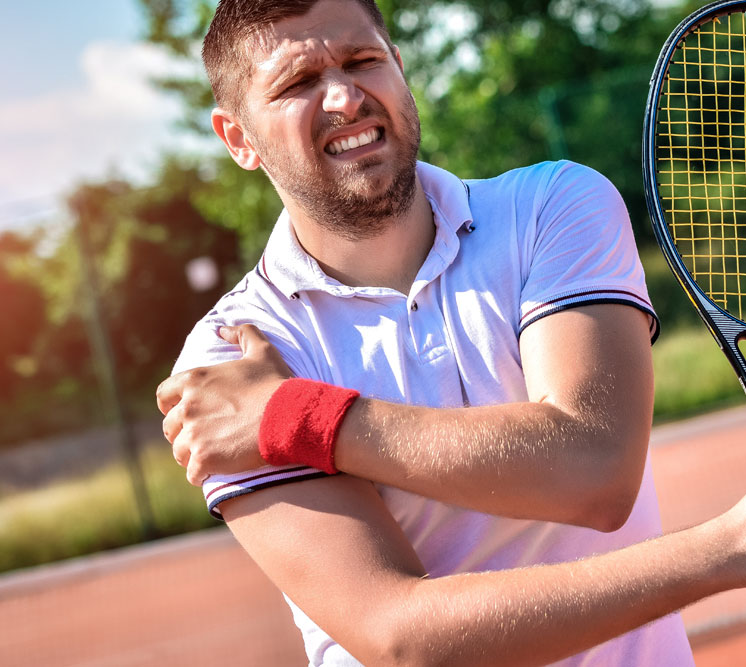 A male tennis player on a court winces in pain as he holds his shoulder, illustrating a sports injury such as a labral tear.