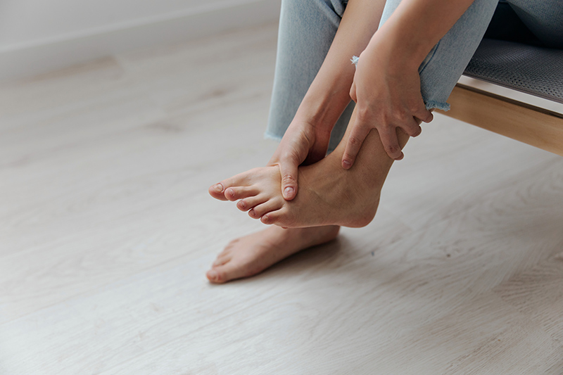 Close-up of a woman holding her foot and ankle while experiencing pain and discomfort.