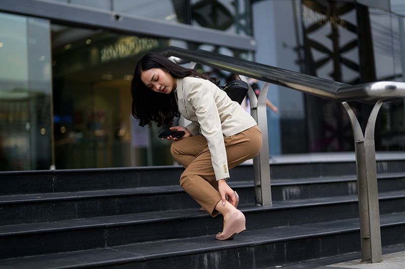 Woman touching her ankle while standing, experiencing discomfort during movement.