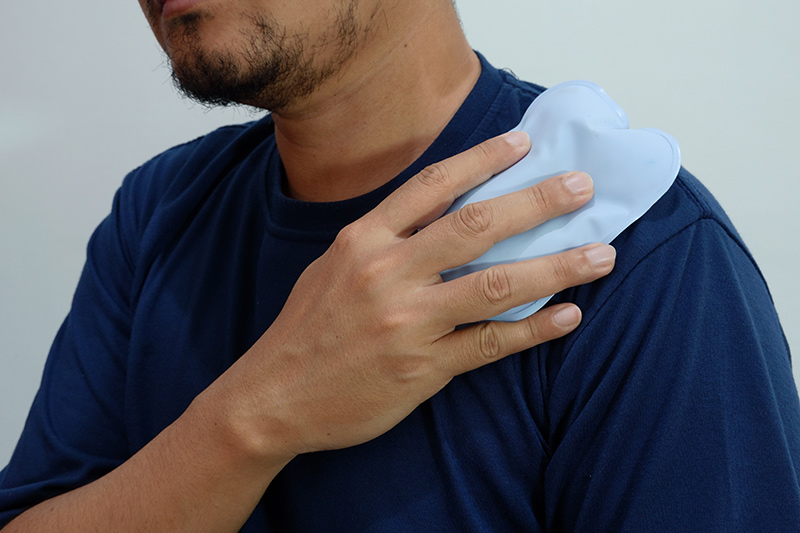 A man self-applying a cold compress onto his shoulder